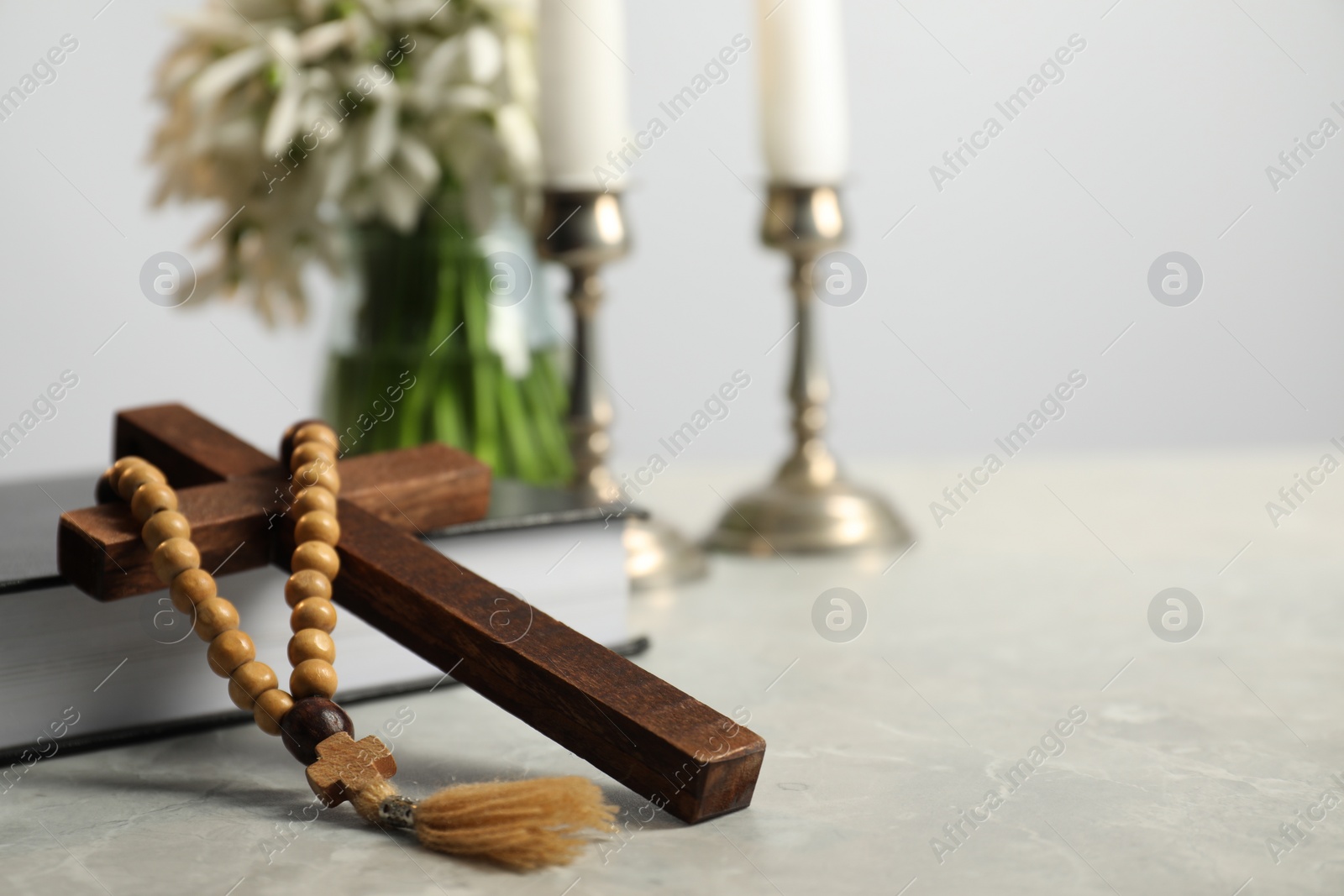 Photo of Wooden cross, rosary beads, Bible and church candles on marble table. Space for text