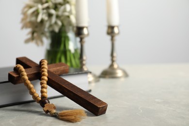 Wooden cross, rosary beads, Bible and church candles on marble table. Space for text