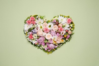 Beautiful heart shaped floral composition on light green background, flat lay