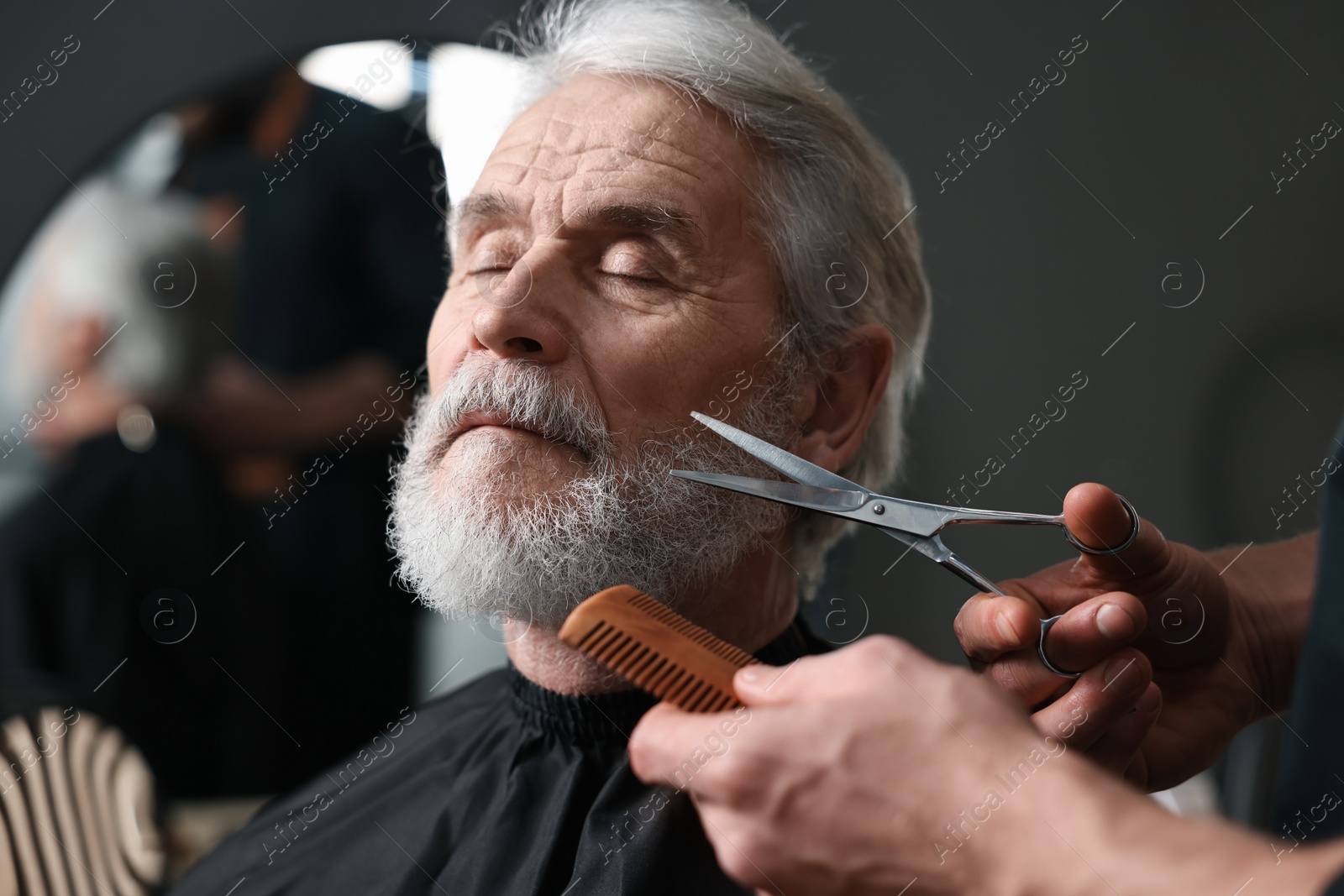 Photo of Professional barber trimming client's beard with scissors in barbershop