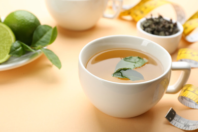 Cup of diet herbal tea with green leaves on orange background