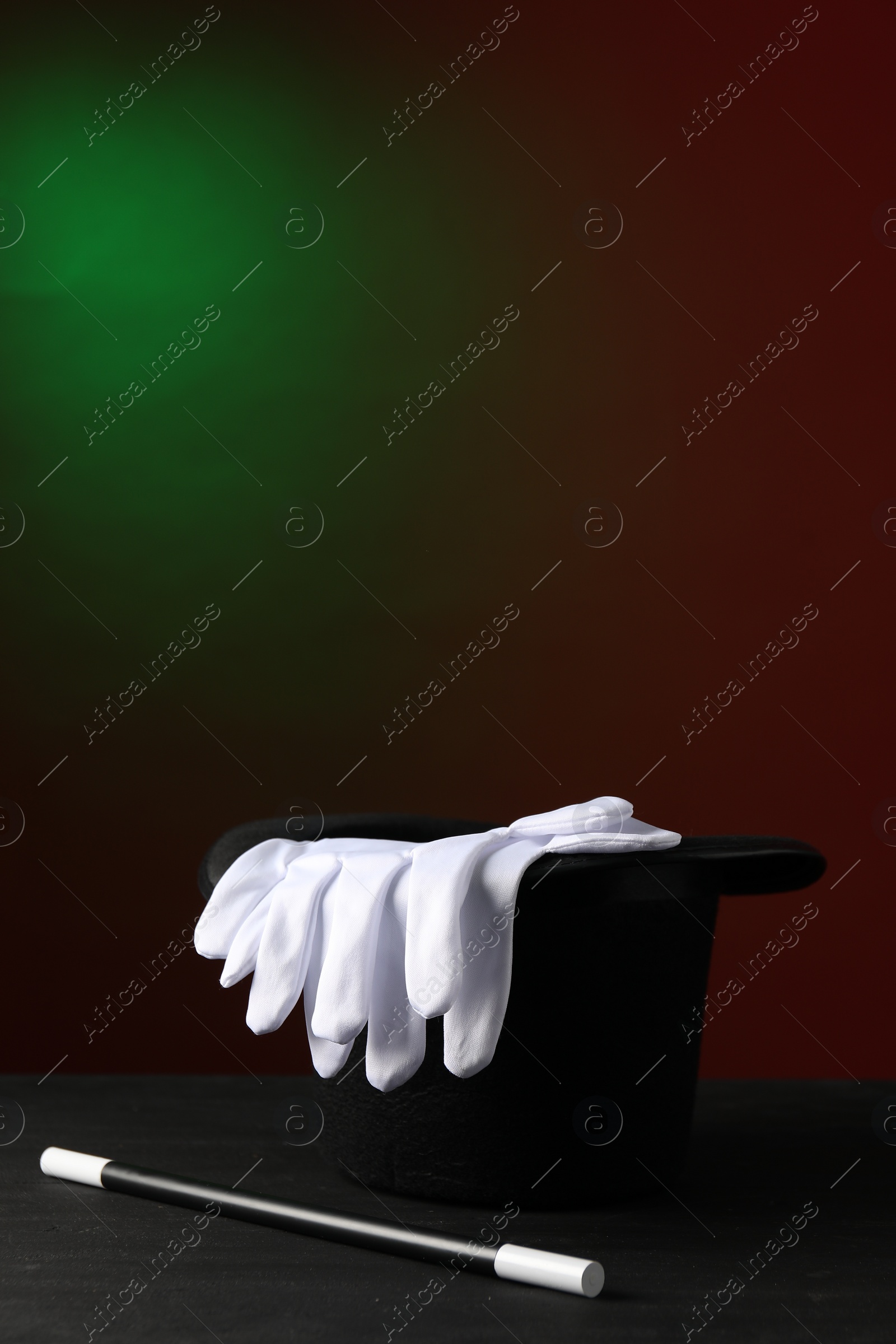 Photo of Magician's hat, wand and gloves on black wooden table against dark background, space for text