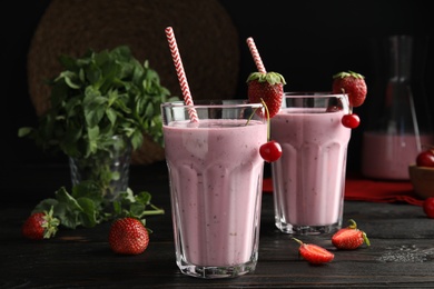 Photo of Tasty fresh milk shakes with berries on black wooden table