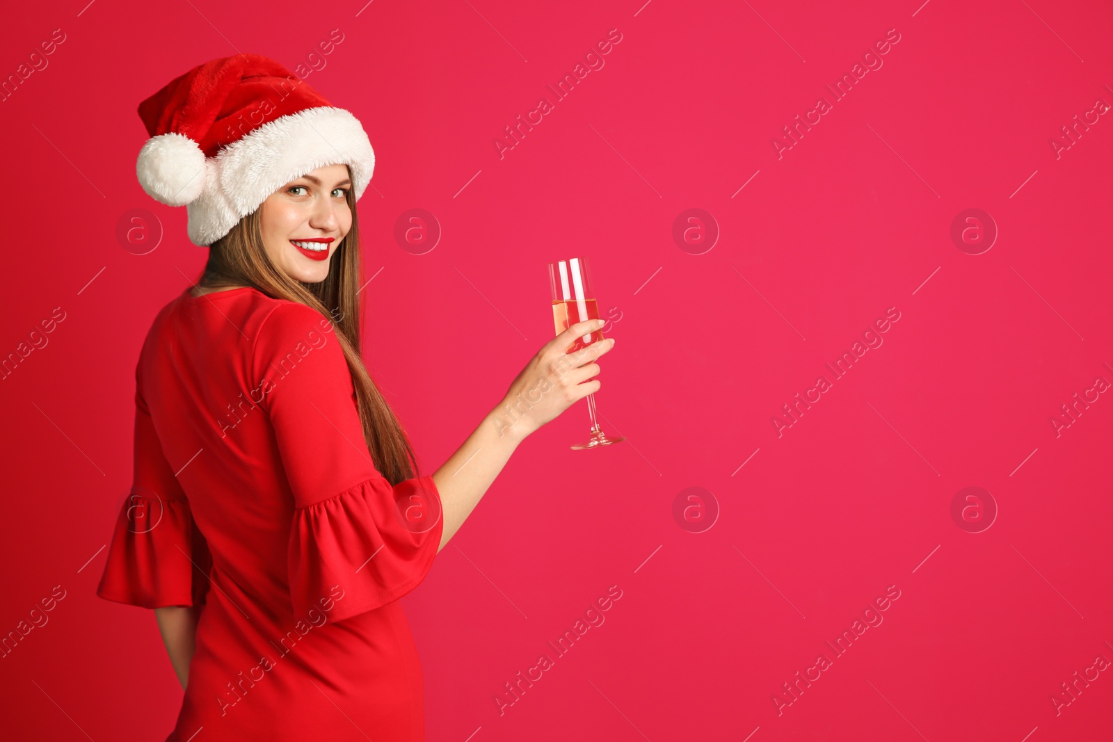 Photo of Young beautiful woman in Santa hat with glass of champagne on color background. Christmas celebration