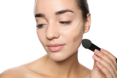 Photo of Young woman applying foundation on her face against white background