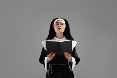 Photo of Nun with Bible praying to God on grey background