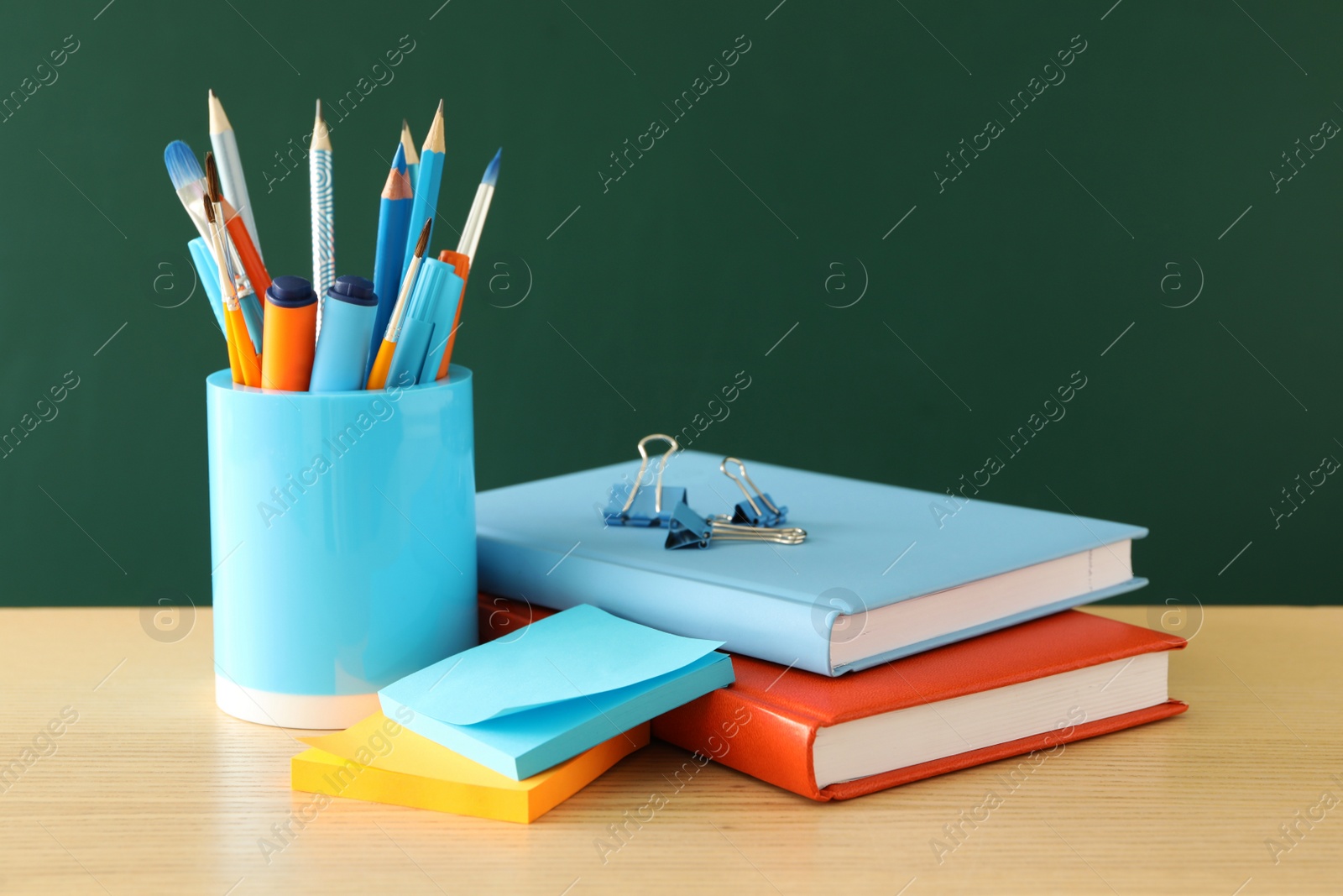 Photo of Different school stationery on wooden table near green chalkboard. Back to school