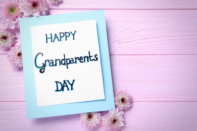 Photo of Beautiful flowers and card with phrase Happy Grandparents Day on pink wooden table, flat lay. Space for text