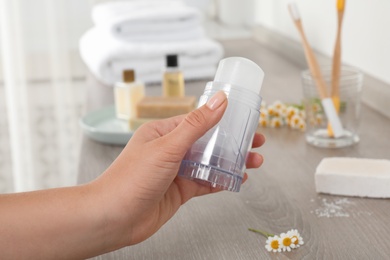 Young woman holding natural crystal alum deodorant at wooden table, closeup