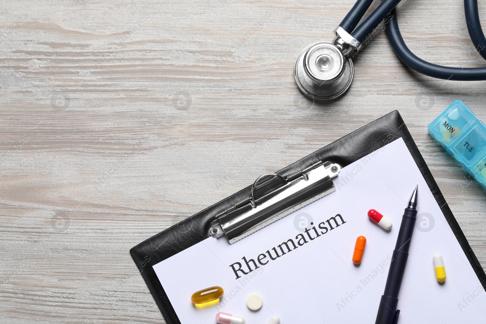 Photo of Clipboard with word Rheumatism, stethoscope and pills on wooden table, flat lay. Space for text