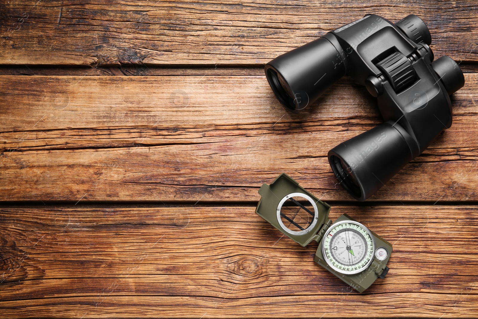 Photo of Binoculars and compass on wooden table, flat lay. Space for text