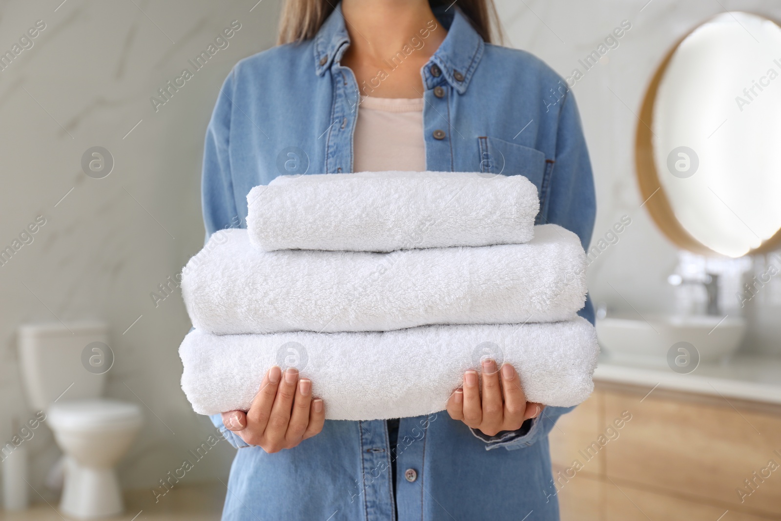 Photo of Woman holding stack of fresh towels indoors, closeup