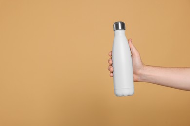 Photo of Man holding thermo bottle with drink on beige background, closeup. Space for text