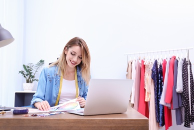 Photo of Beautiful young stylist at workplace near rack with clothes