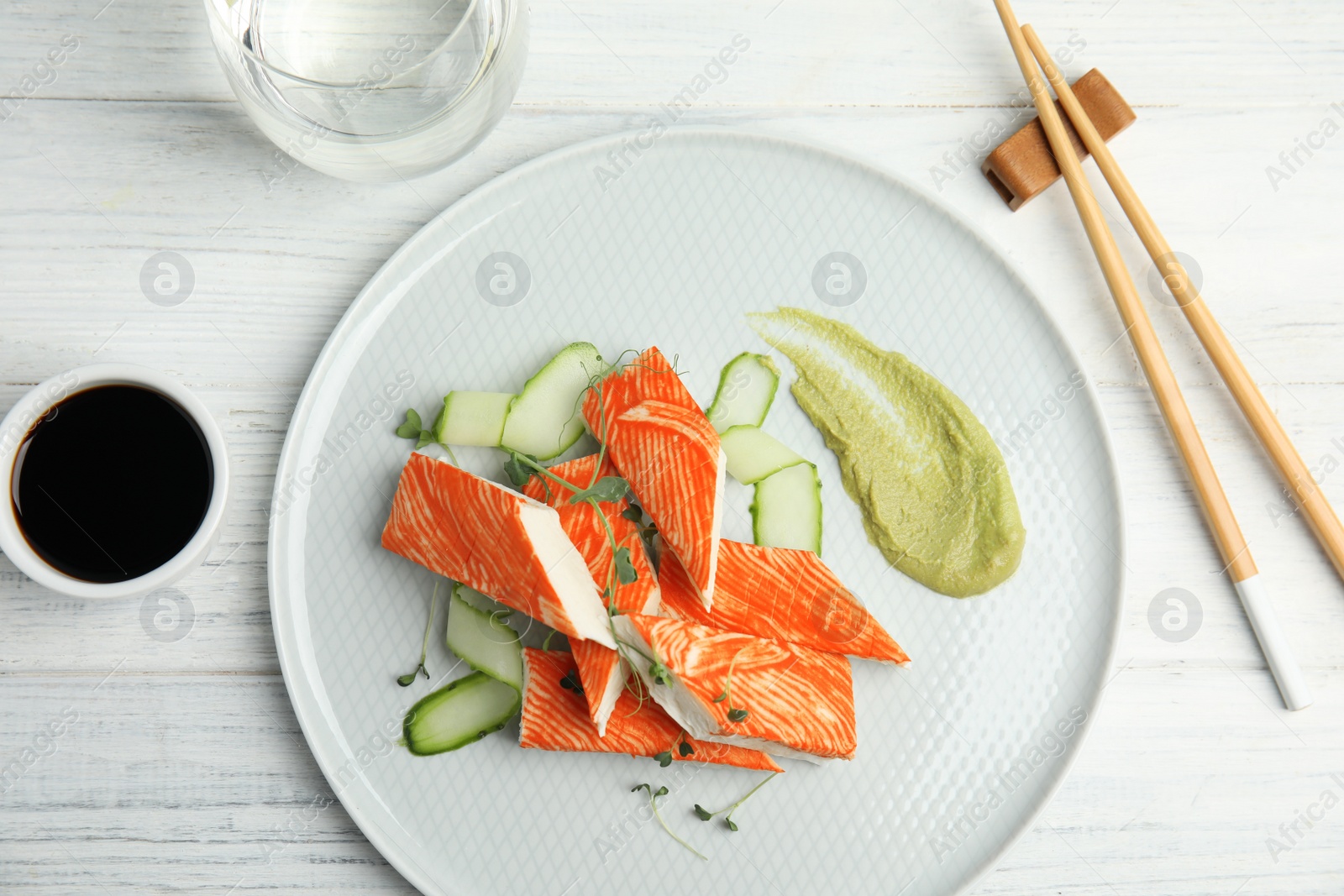 Photo of Fresh crab sticks with cucumber and soy sauce on white wooden table, flat lay