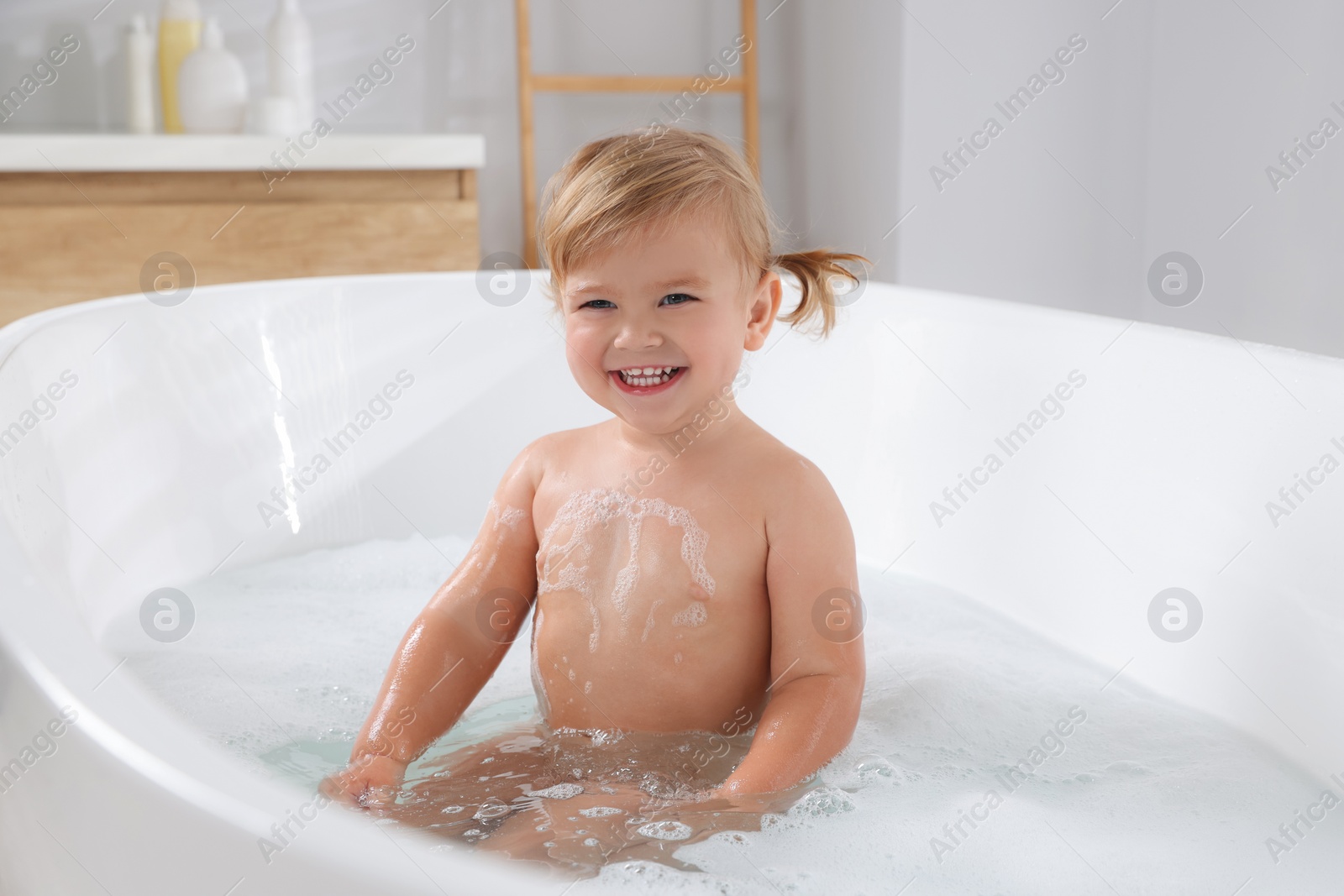 Photo of Cute little girl taking foamy bath at home