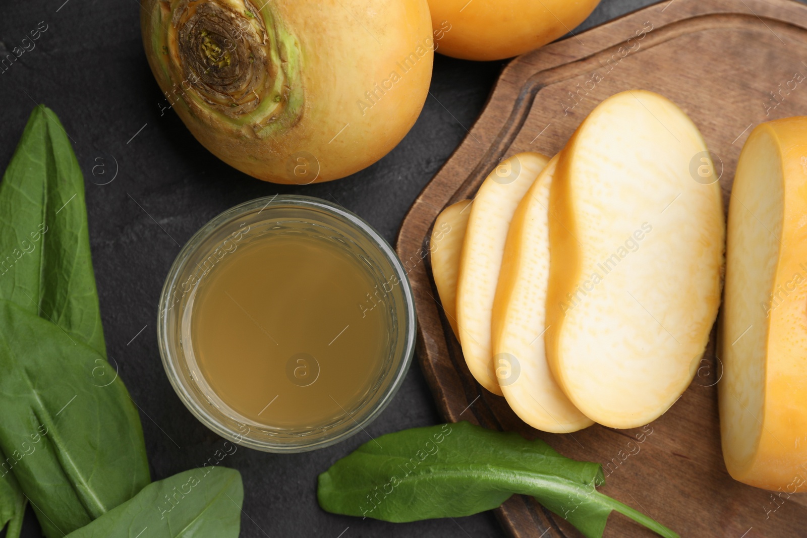 Photo of Glass of fresh natural turnip juice, green leaves, cut and whole roots on black table, flat lay