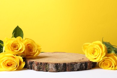 Photo of Beautiful presentation for product. Wooden stump and roses on white table against yellow background, space for text