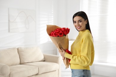 Photo of Happy woman with red tulip bouquet at home, space for text. 8th of March celebration