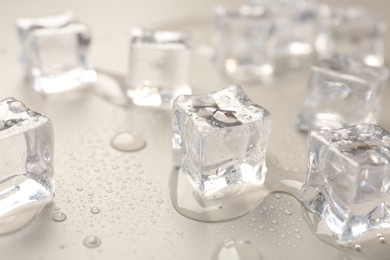 Photo of Melting ice cubes and water drops on light grey background, closeup