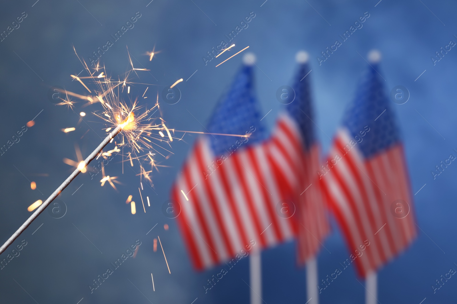 Photo of Burning sparkler against USA flags, closeup with space for text. Happy Independence Day