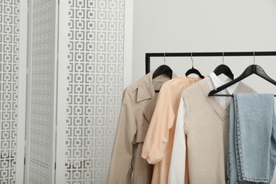 Photo of Rack with different stylish women's clothes and folding screen near light wall