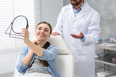 Photo of Young woman looking at her new dental implants in mirror indoors