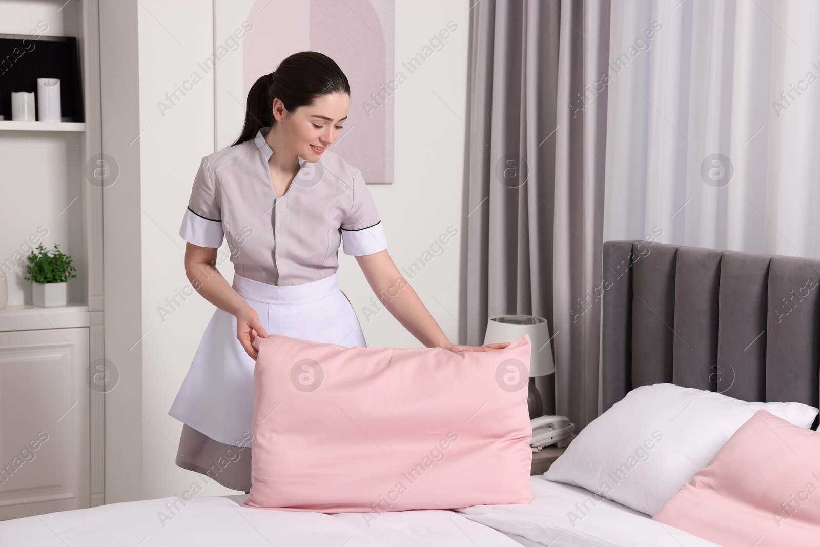 Photo of Young maid making bed in hotel room