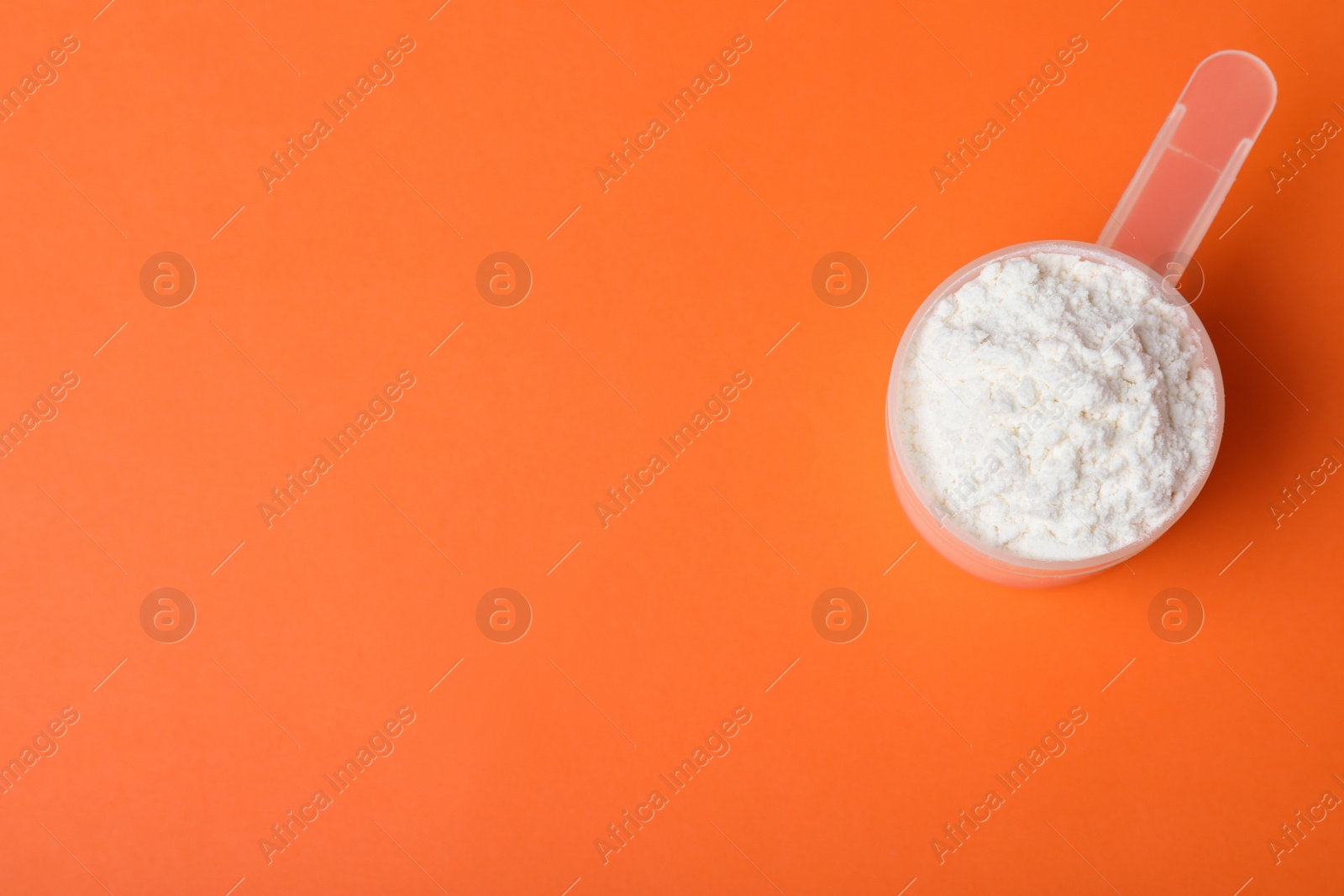 Photo of Scoop of protein powder on orange background, top view with space for text