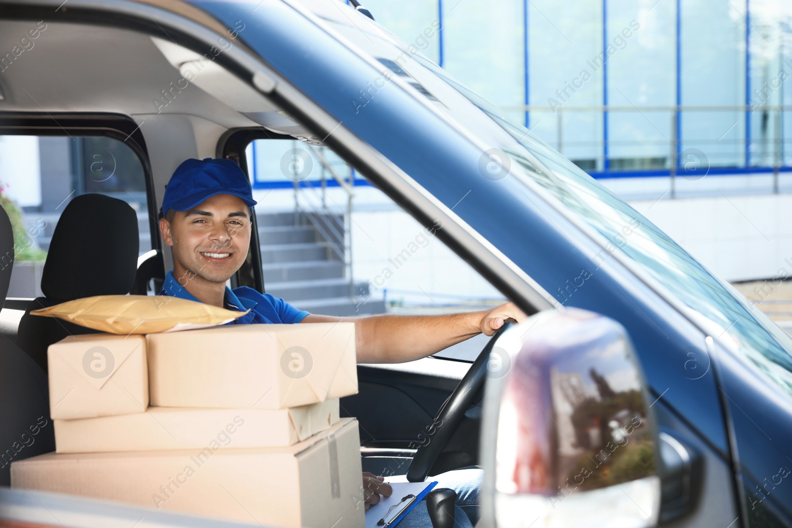 Photo of Young courier with parcels in delivery car