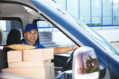 Photo of Young courier with parcels in delivery car