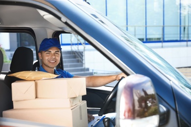 Young courier with parcels in delivery car