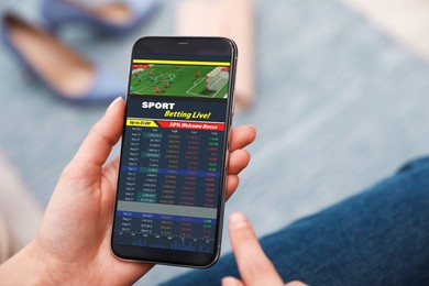 Woman betting on sports using smartphone, closeup. Bookmaker website on display