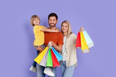 Photo of Family shopping. Happy parents and son with many colorful bags on violet background