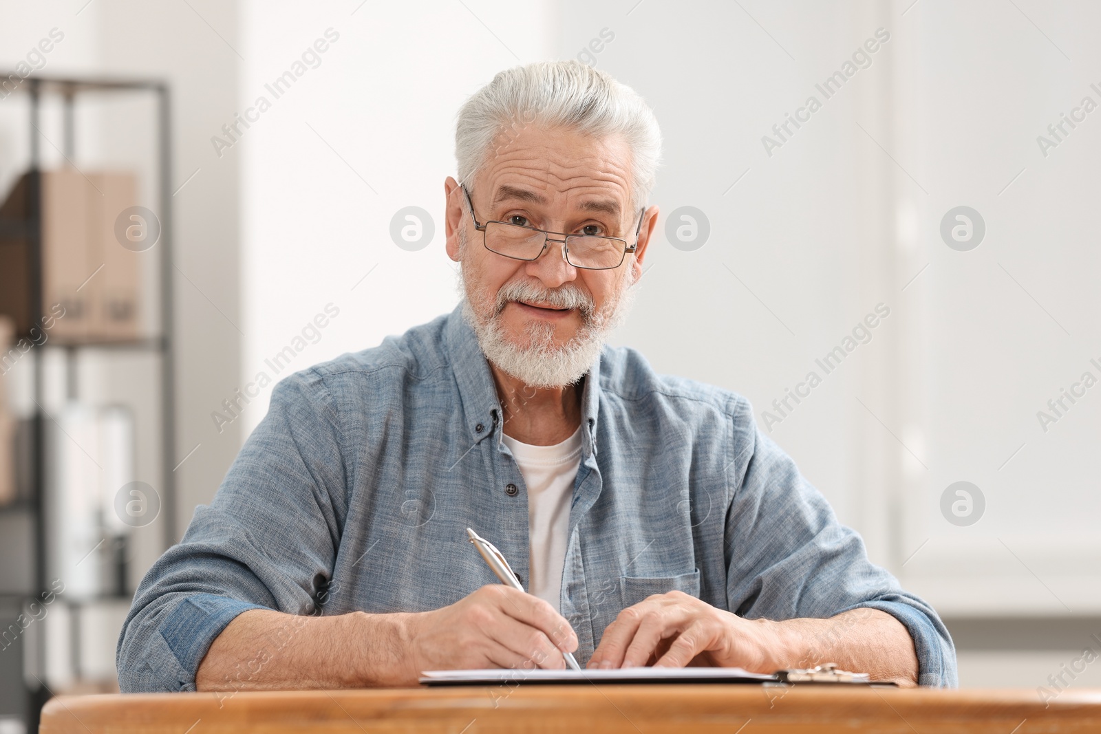 Photo of Senior man signing Last Will and Testament at table indoors