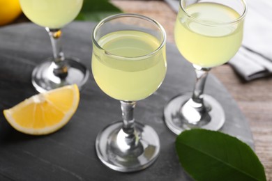 Photo of Tasty limoncello liqueur, lemon slice and green leaf on table, closeup