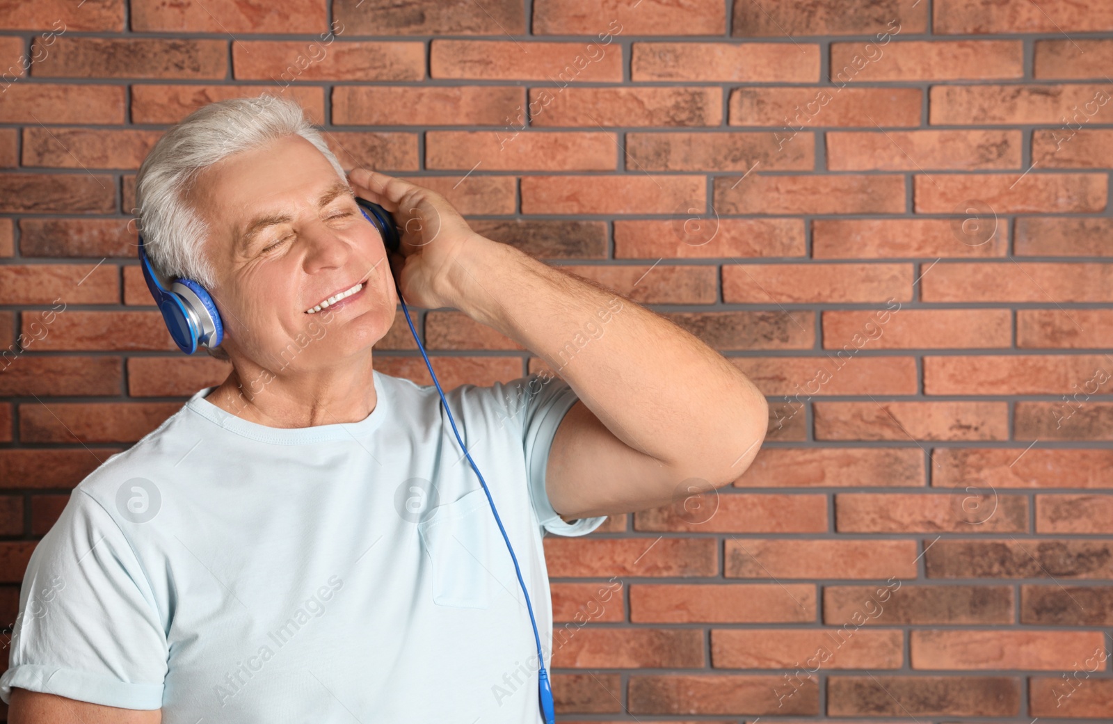 Photo of Mature man enjoying music in headphones against brick wall. Space for text