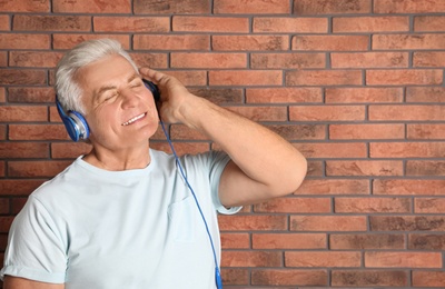Mature man enjoying music in headphones against brick wall. Space for text