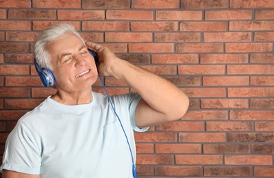 Photo of Mature man enjoying music in headphones against brick wall. Space for text