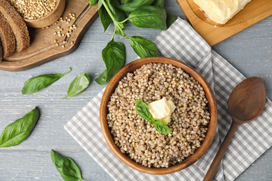 Photo of Tasty buckwheat porridge with butter on grey wooden table, flat lay