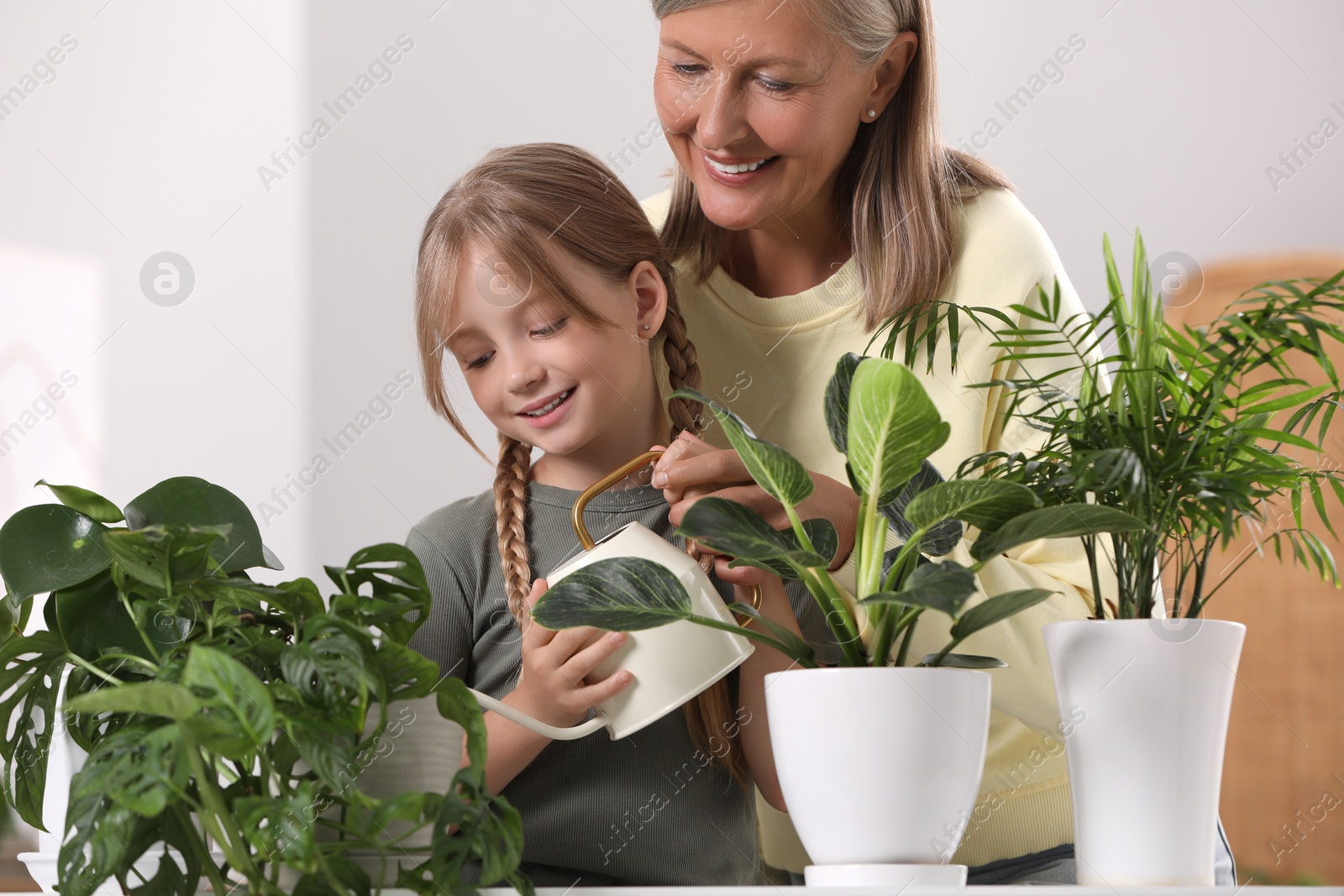 Photo of Grandmother with her granddaughter watering houseplants together at home