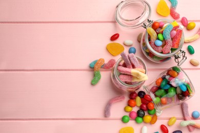 Photo of Jars with different delicious candies on pink wooden table, flat lay. Space for text