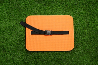 Orange foam seat mat for tourist on green grass, top view