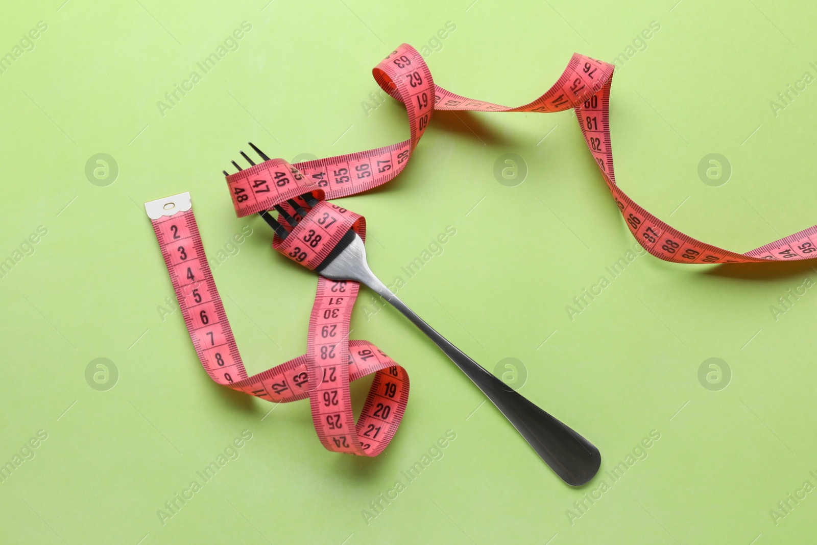 Photo of Fork with measuring tape on light green background, top view. Diet concept