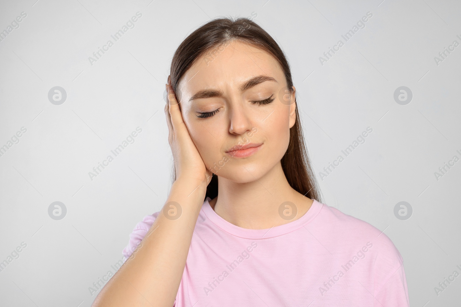 Photo of Young woman suffering from ear pain on light grey background