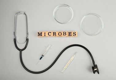 Photo of Word Microbes made with wooden cubes, stethoscope and syringe on light background, flat lay
