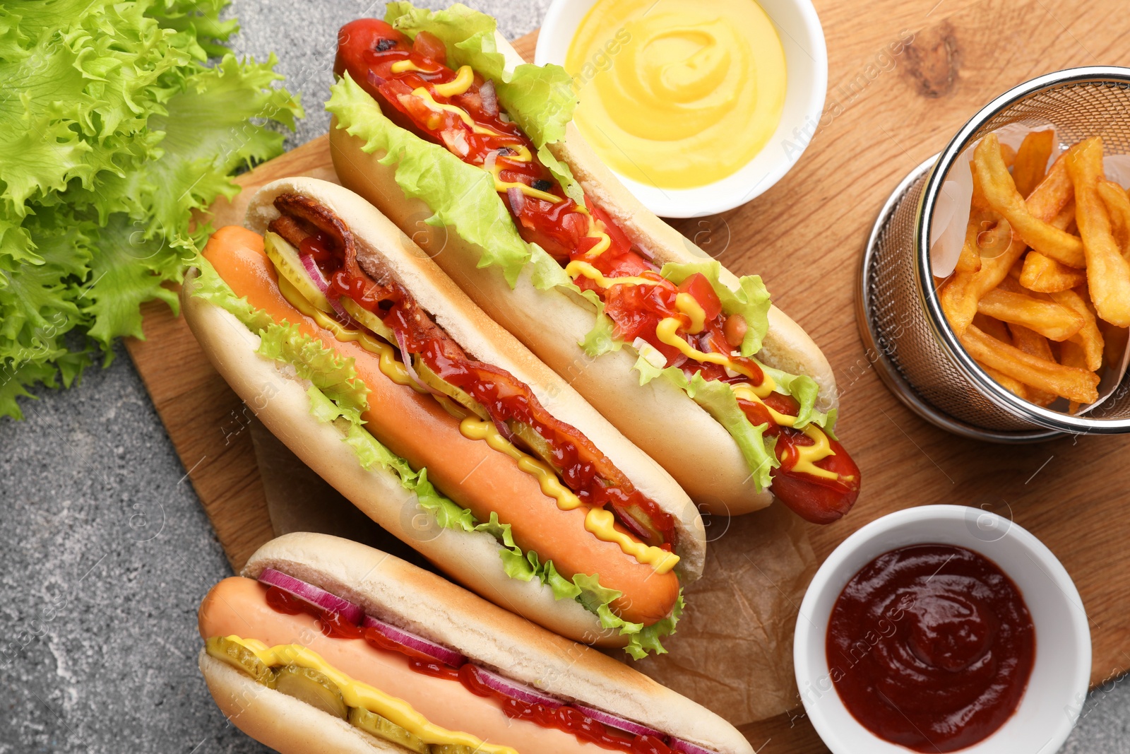 Photo of Delicious hot dogs with different toppings served on grey table, flat lay