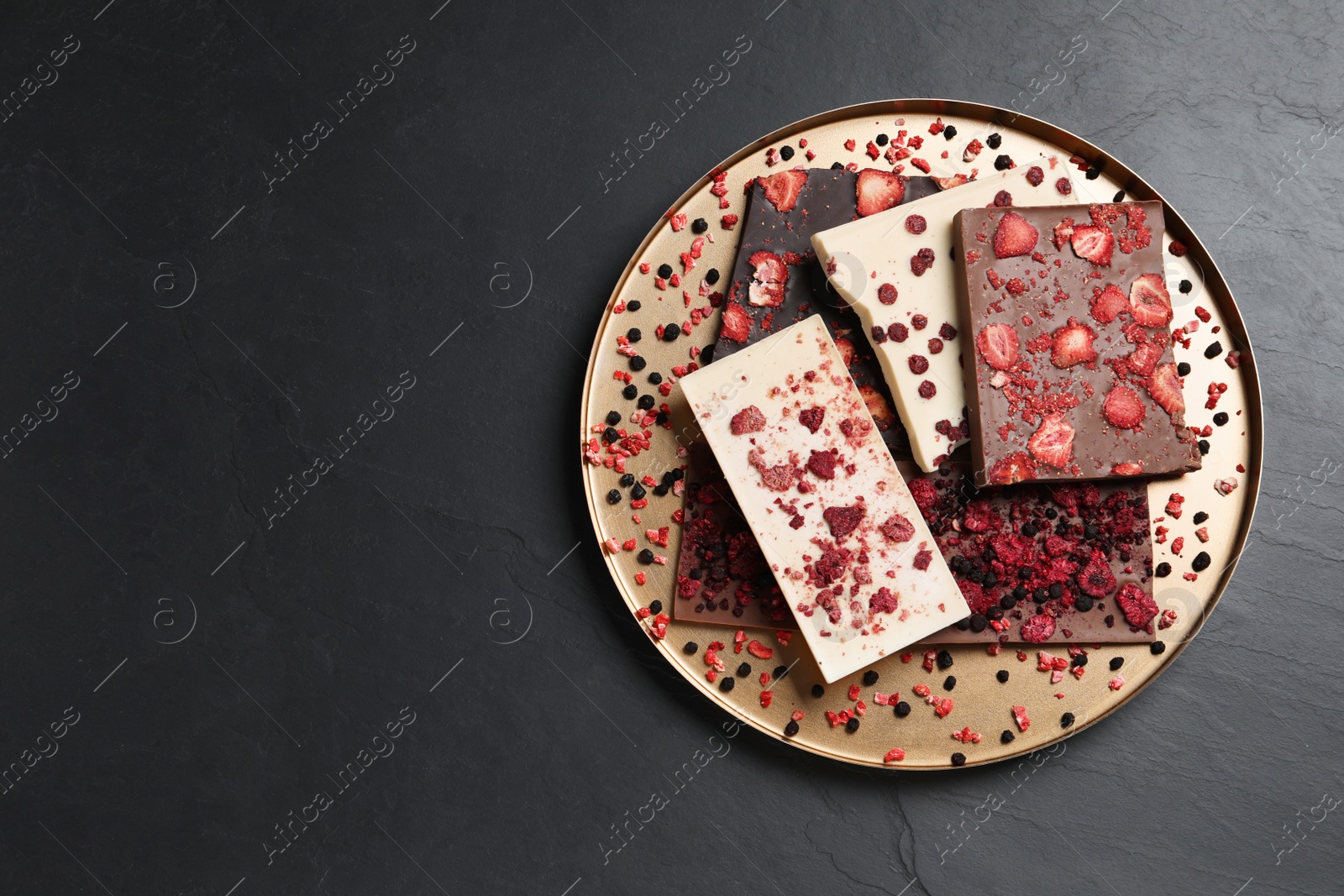 Photo of Different chocolate bars with freeze dried fruits on black table, top view. Space for text