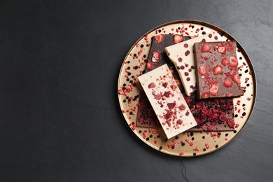 Different chocolate bars with freeze dried fruits on black table, top view. Space for text