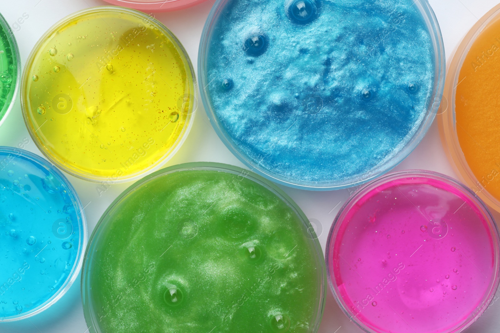 Photo of Colorful slimes in plastic containers on white background, top view. Antistress toy